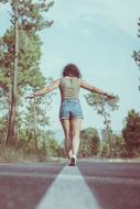 Back view of the girl, balancing on the white line, among the road