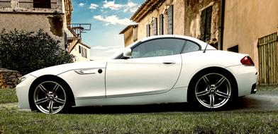 Side view of the beautiful, shiny, white "BMW Z4" car, on the green grass, among the buildings