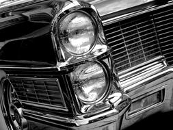 Black and white photo with the close-up of the headlights of the beautiful, retro Cadillac Coupe Deville car