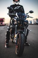 Guy in helmet and equipment, on the motorcycle, on the asphalt, at colorful sunset