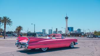 Beautiful, shiny, vintage, pink car with the lines, near the tower, buildings and plants