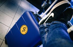 Man in jeans and "Nike" shoes, with the blue and yellow trolley, in the airport