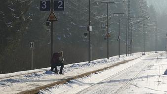 Person, sitting near the beautiful, snowy railway, near the road, among the trees, in sunlight, in the winter