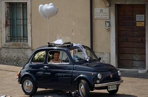 Beautiful, shiny, black Flat 500 wedding car with decorations, with the bride and groom, near the building