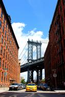 Beautiful landscape with the cars, among the buildings and Brooklyn Bridge in New York, USA, at blue sky with white clouds on background