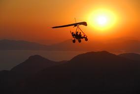 Silhouette of the people, on the flying vehicle, above the mountains, at colorful and beautiful sunset