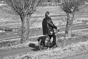 Black and white photo of the man cyclist on the beautiful road with trees, among the fields