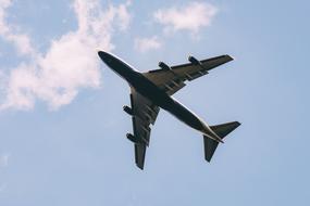 Flying airplane, under the blue sky with white clouds, from the bottom view