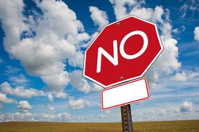 Red and white "NO" sign, near the colorful and beautiful field, at blue sky with white clouds on background