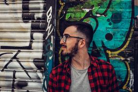 Profile portrait of a bearded man, with the glasses, near the wall, with the colorful graffities