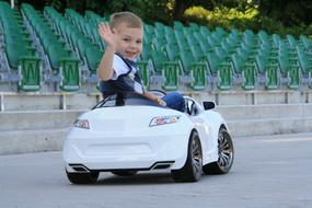 Child boy waving his hand in the white toy car