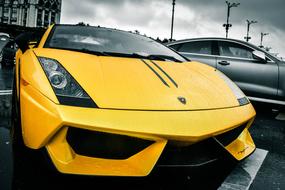 Front of the beautiful, shiny, yellow "Lamborghini" car, near the other shiny car, under the clouds