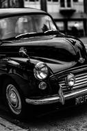 Black and white photo of the beautiful, shiny, black, vintage car, near the building