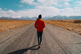 man walks along an empty road in the desert