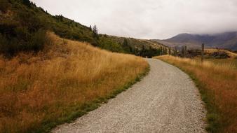 gravel road near a hill with dry grass