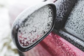 Close-up of the beautiful, frozen mirror of the red car, in winter