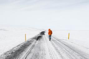 man in an orange jacket on an empty snowy road