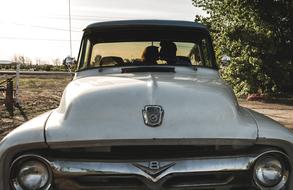 Front of the beautiful, retro, American Ford car in light, near the green trees