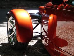 Close-up of the shiny, vintage, orange racing car, in light, with the reflections