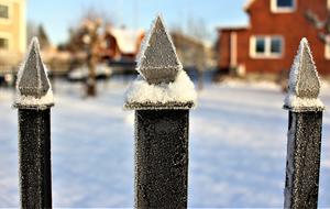 Close-up of the iron fence, in the beautiful rime, among the snowy houses, in winter