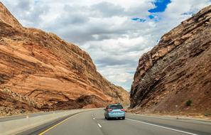 Beautiful landscape of the road, with the car, among the mountains, under the blue sky with white clouds, in Utah, USA