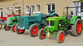 Colorful oldtimer tractors on the parade, near the building, in light