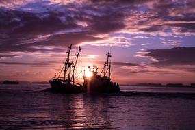 silhouettes of ships on the water in pink twilight