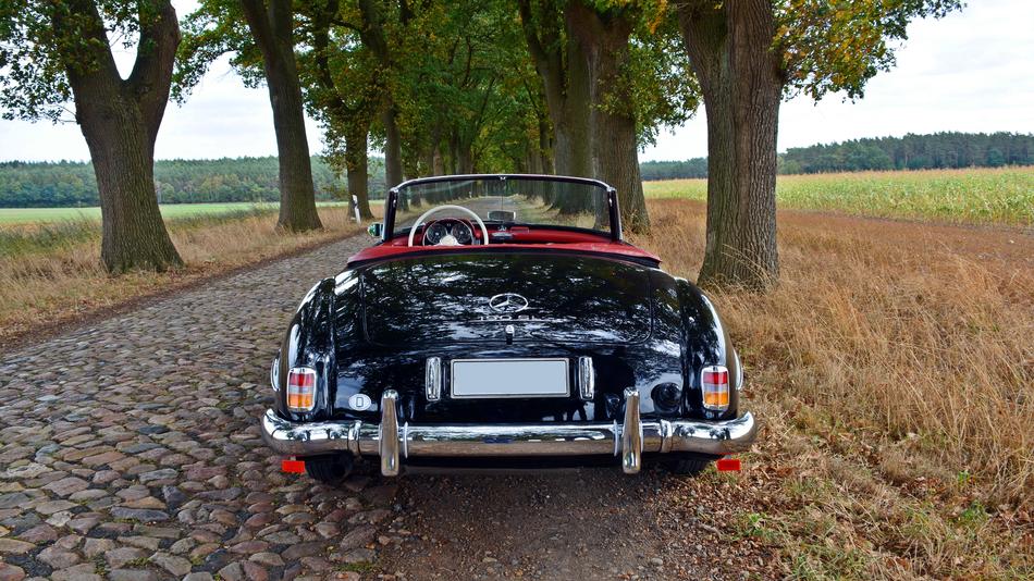 Beautiful, shiny, black and red Mercedes 190 Sl, on the road, among the colorful and beautiful fields and trees