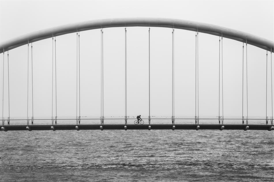 black and white photo of a biker on a suspension bridge