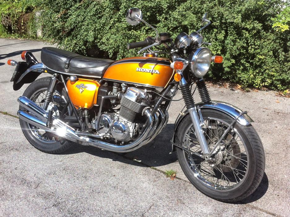 Orange and black, shiny Honda Cb 750 motorcycle on the asphalt, near the green plants