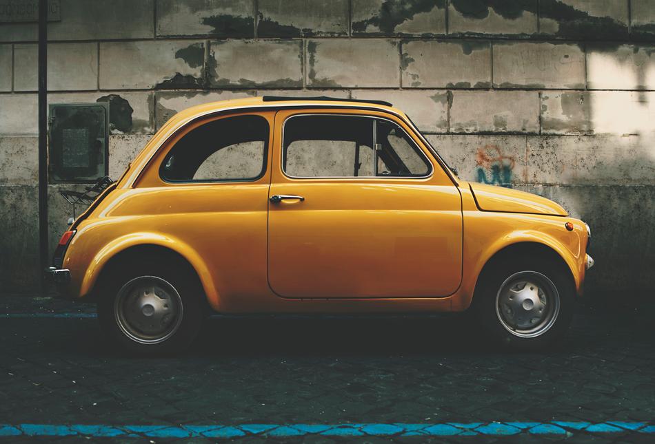 small vintage Yellow Car parked at brick wall