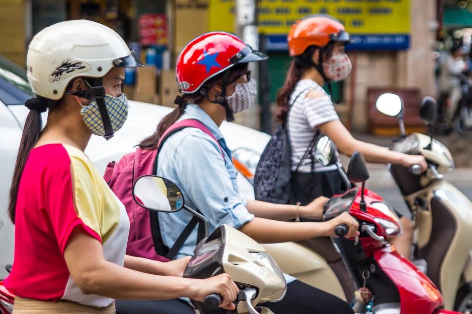 Girls on the scooters, with the equipment, on the road, near the buildings, in Hanoi, Vietnam