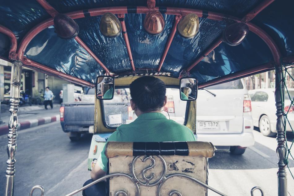 Back view of a man, sitting in the vehicle, on the road, among the cars, people and buildings, in Thailand