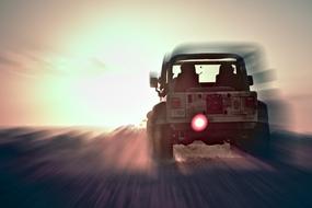 People in the Jeep Wrangler on the road, in motion, at colorful sunset