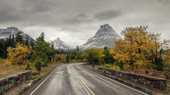 Beautiful landscape of the road and valley with snowy mountains, under the cloudy sky, in autumn