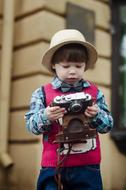 Cute child in hat, with the camera, near the building, on the street, in the rain