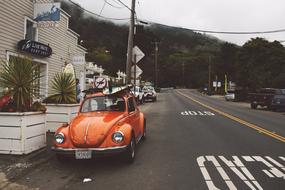 Beautiful landscape of the road with orange, retro Volkswagen Beetle car near the buildings, near the mountains