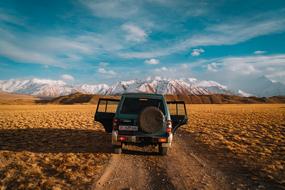 jeep on a dirt road at the foot of the snow-capped mountains
