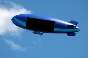 Flying, blue blimp with advertisement, under the blue sky with white clouds