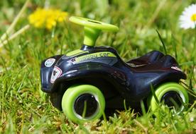 Shiny, colorful car toy among the beautiful and colorful flowers and green grass, in sunlight
