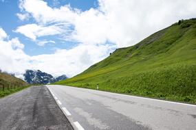 asphalt road near a hill with green grass