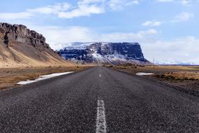 Beautiful landscape of the road, among the colorful fields, near the snowy mountain, under the blue sky with white clouds