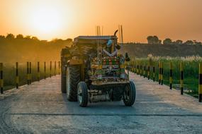 Tractor on the bridge among the green plants, at beautiful, orange sunset