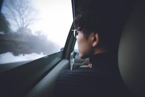 Guy in glasses, looking out of the car window, on the beautiful plants in snow and fog