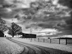 Beautiful, black and white landscape with the barn among the plants and fields, under the cloudy sky