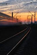 Landscape of the shiny railway with the train movement, at colorful and beautiful sunset with clouds