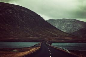 Beautiful landscape with the road, among the water and colorful mountains, under the clouds