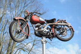 Colorful, vintage motorcycle on the pole in sunlight, near the trees, under the blue sky with white clouds