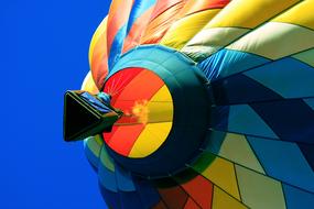 Flying, colorful, patterned hot air balloon with shapes, in sunlight, under the blue sky