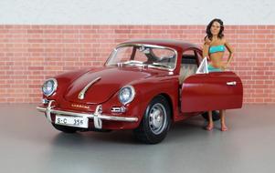 Model of the girl near the shiny, red model of "Porsche 356" car, near the brick wall